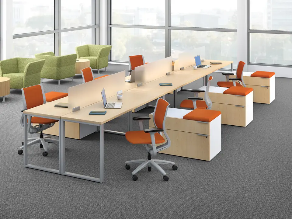 Open-plan benching workstations with orange task chairs and a lounge area
